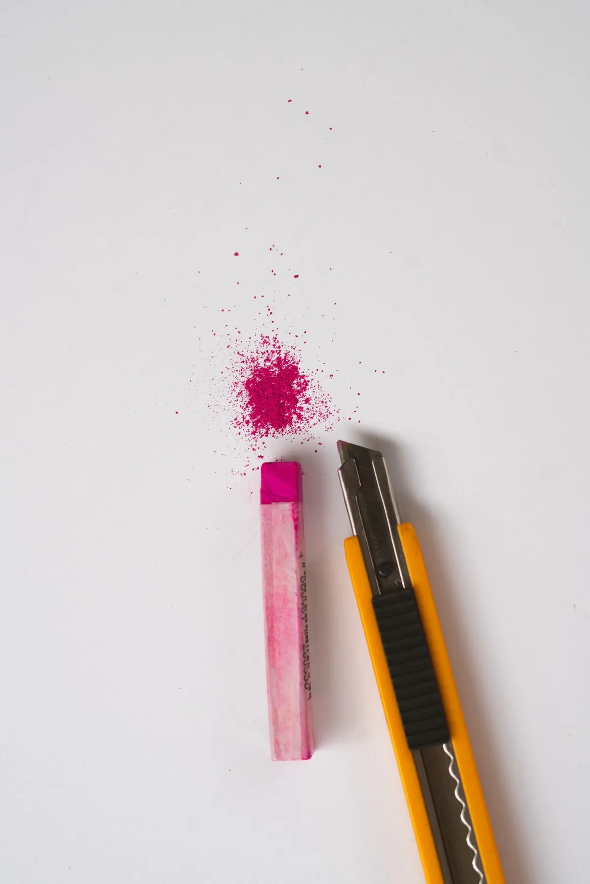 A pink pastel stick and craft knife with a dusting of pink pigment